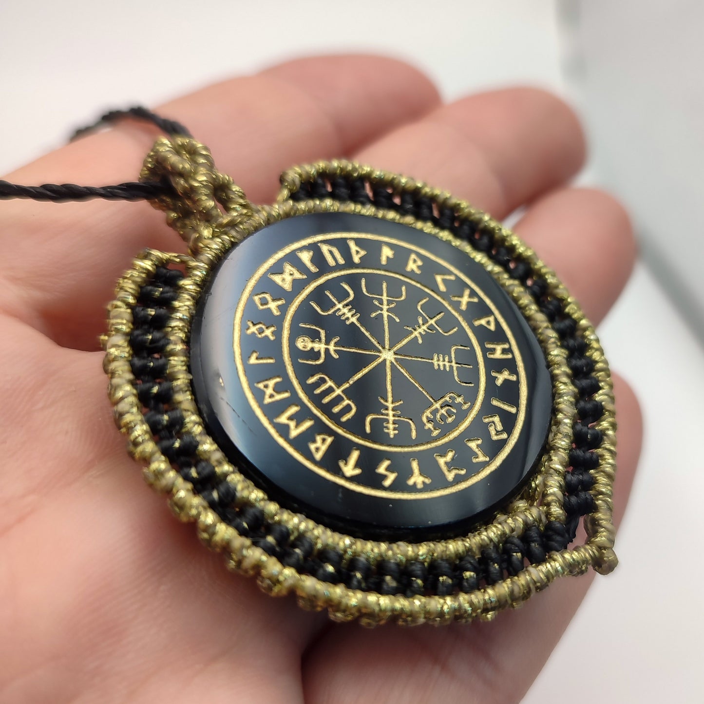 Detalle del tejido artesanal en negro y oro rodeando la piedra protectora.