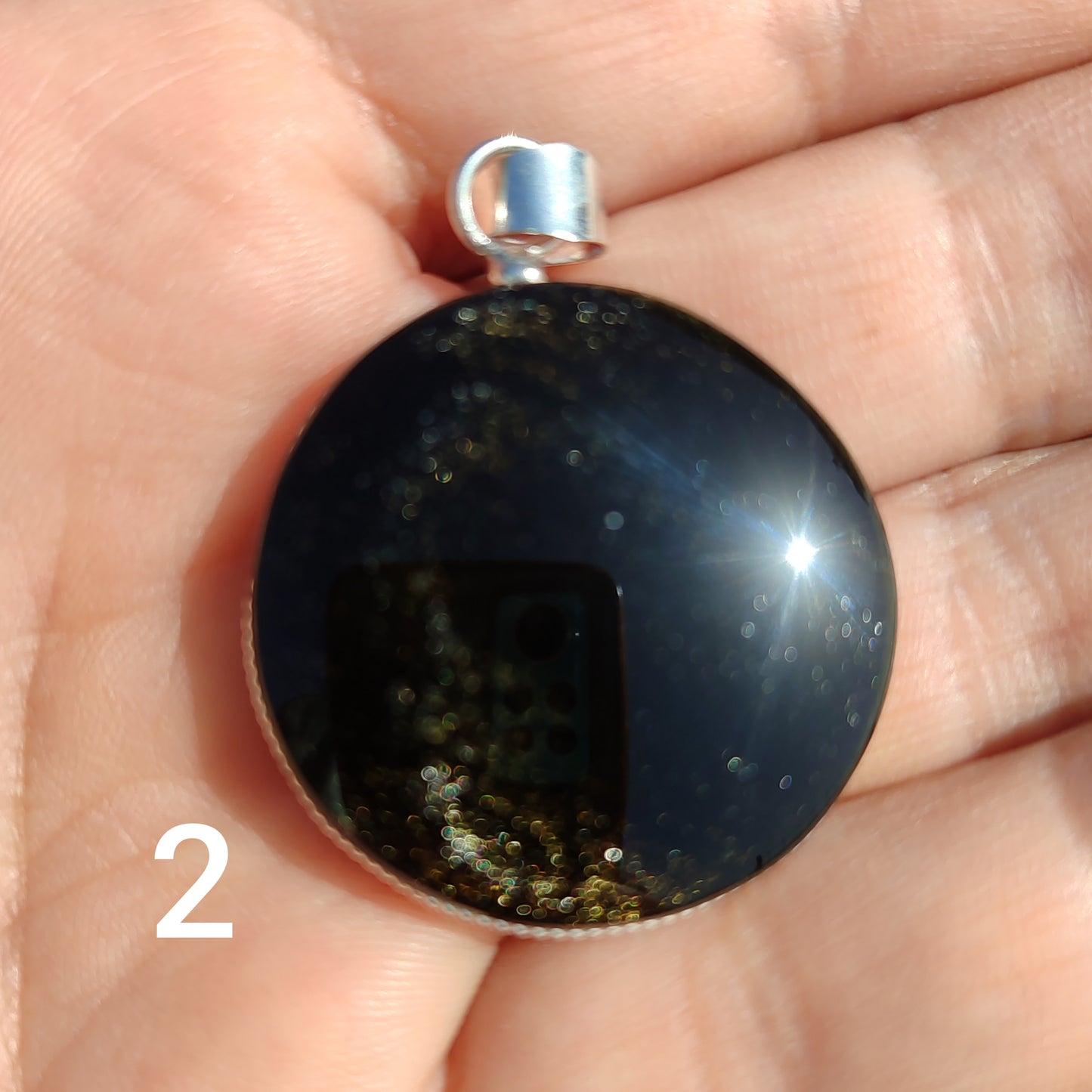 Colgante circular de obsidiana dorada natural con reflejos dorados sobre la palma de la mano