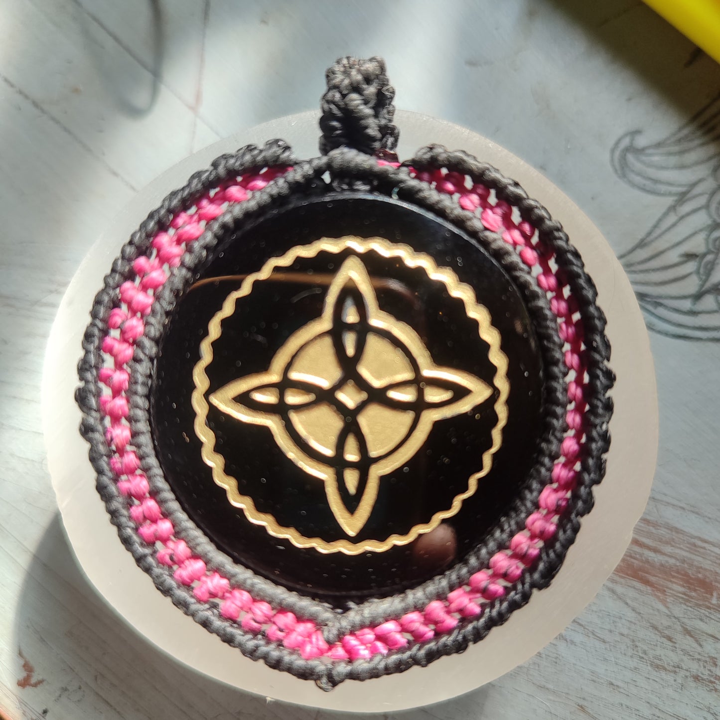 Colgante Nudo de Bruja grabado en dorado sobre espejo de obsidiana negra.