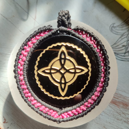 Colgante Nudo de Bruja grabado en dorado sobre espejo de obsidiana negra.