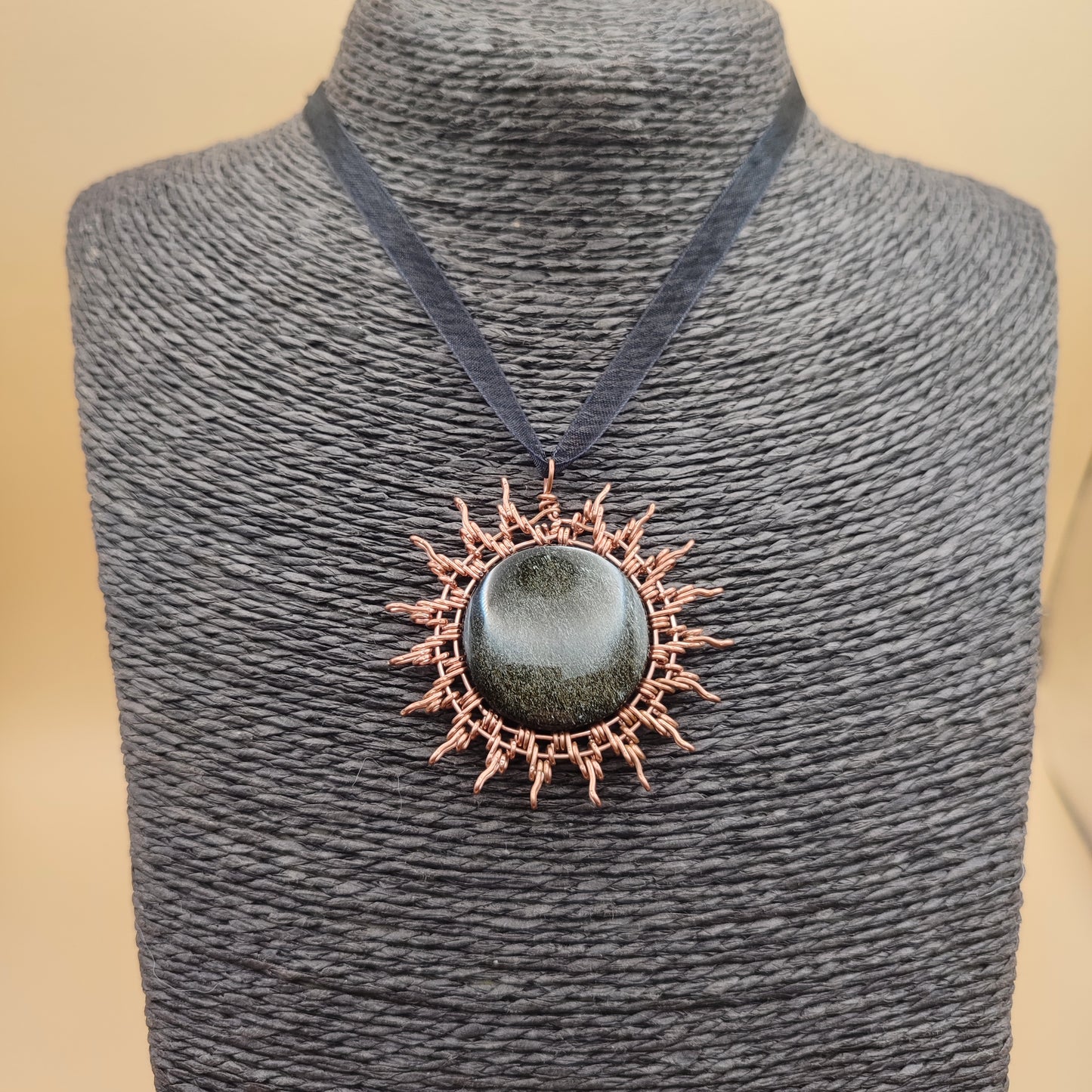 Colgante de cobre artesanal en forma de sol con piedra obsidiana dorada.