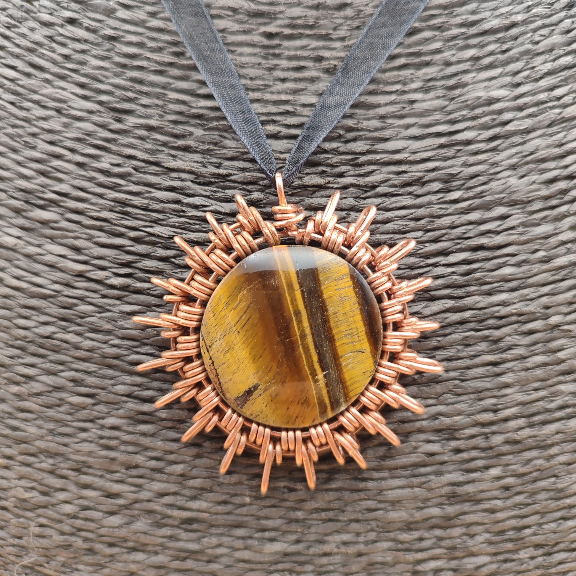 Colgante artesanal de cobre en forma de sol con piedra ojo de tigre natural