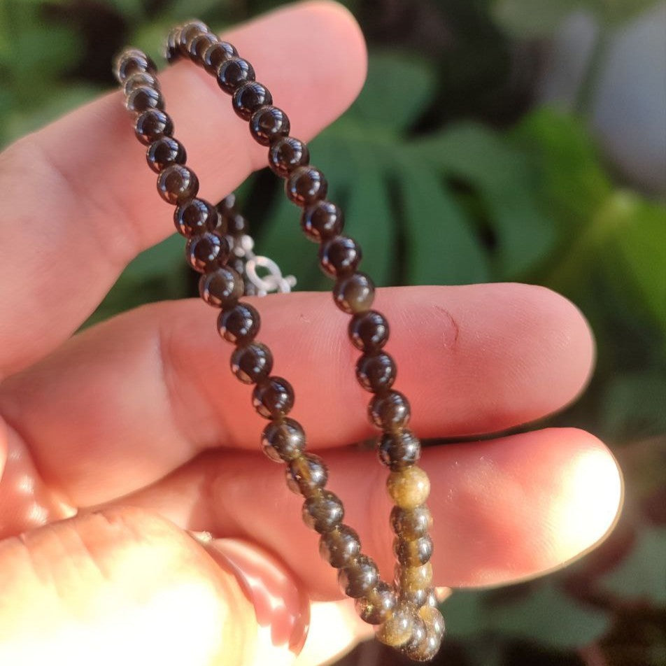 Detalle del collar de obsidiana dorada sujeto en la mano.