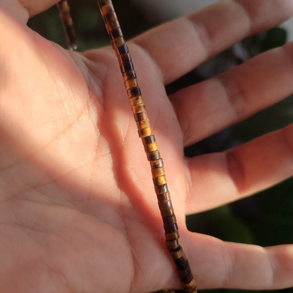 Collar de ojo de tigre sujeto en la mano resaltando su diseño estructural.