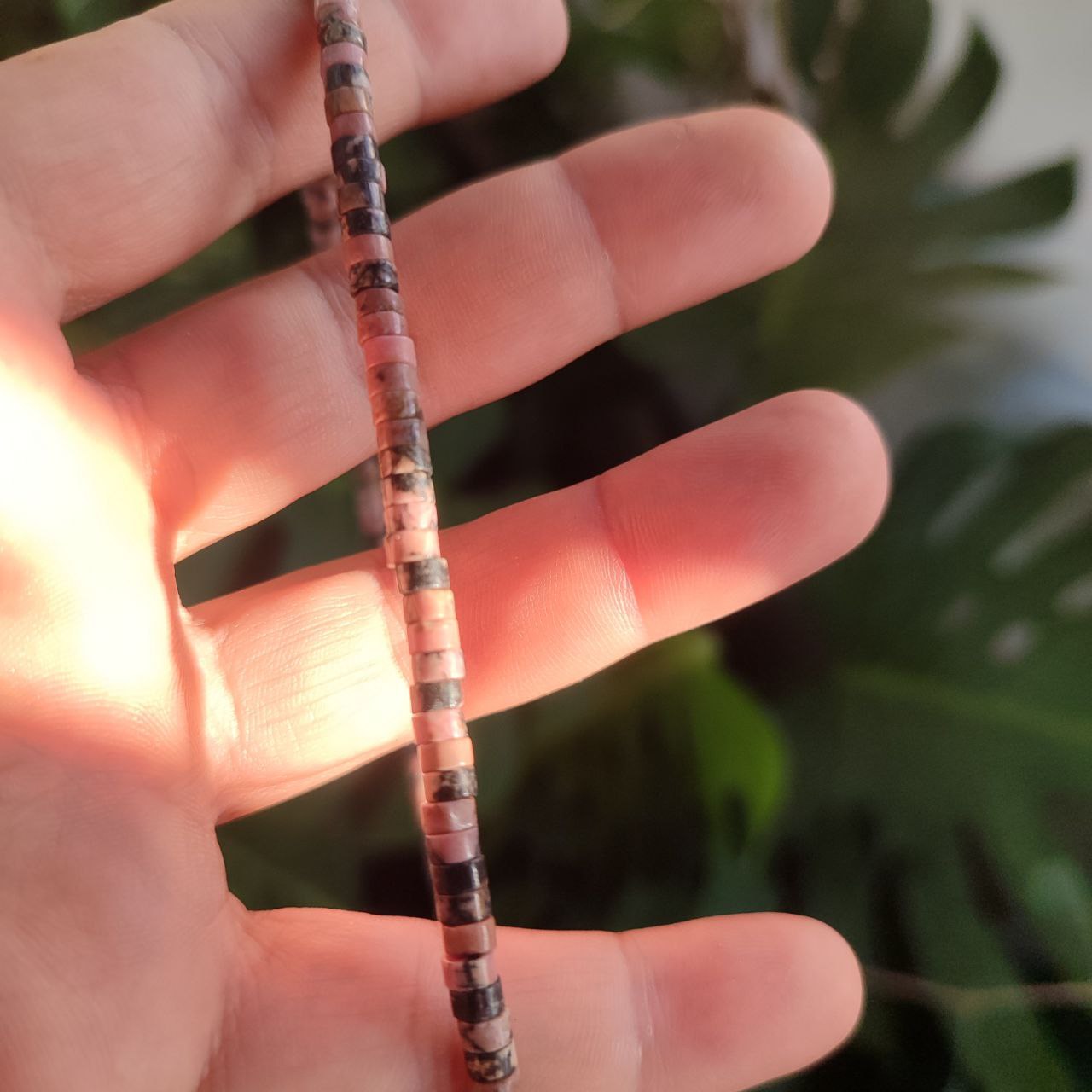 Collar de rodonita natural sujeto en la mano mostrando su estructura de disco.