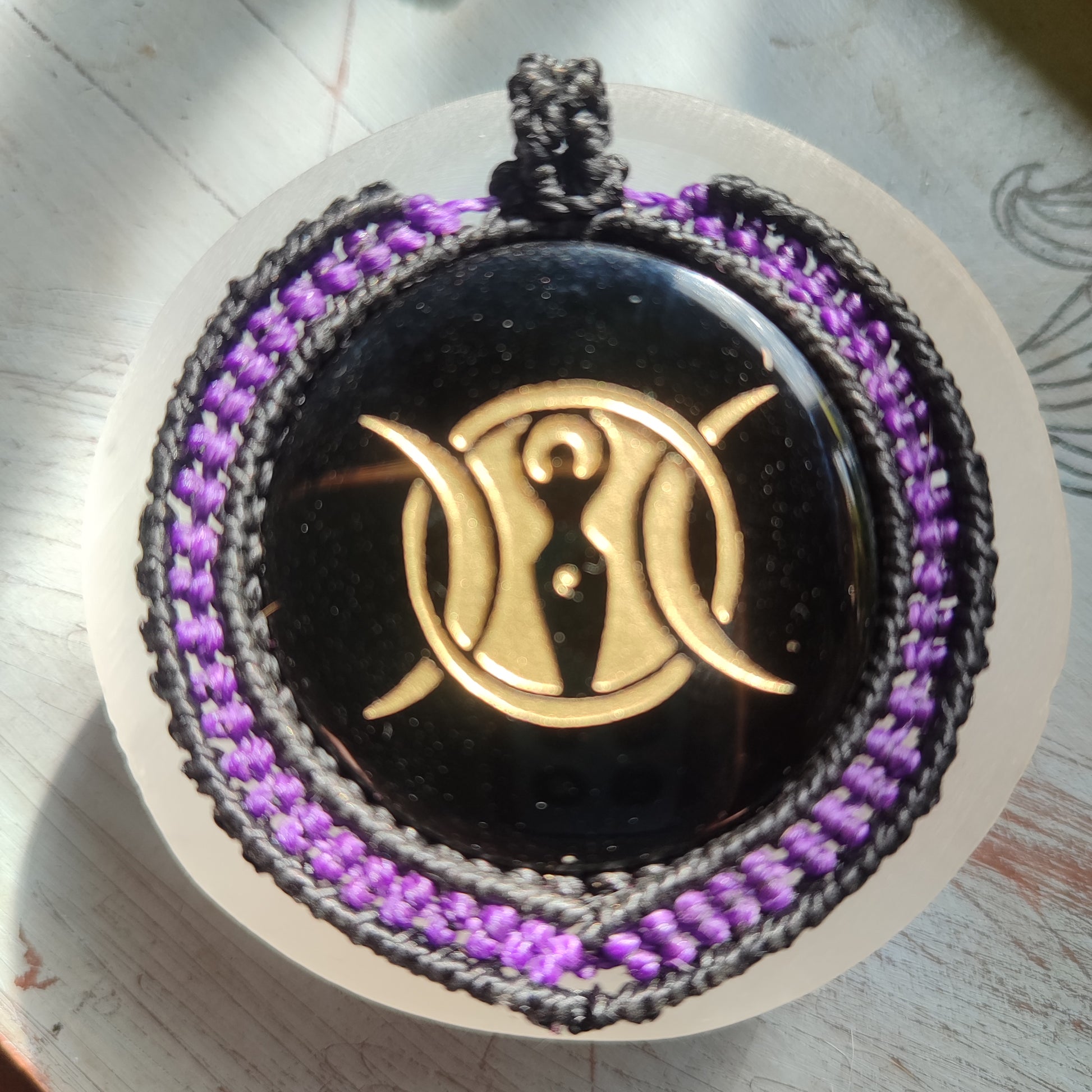 Primer plano del grabado místico de la Triple Diosa sobre el brillo de la obsidiana negra.