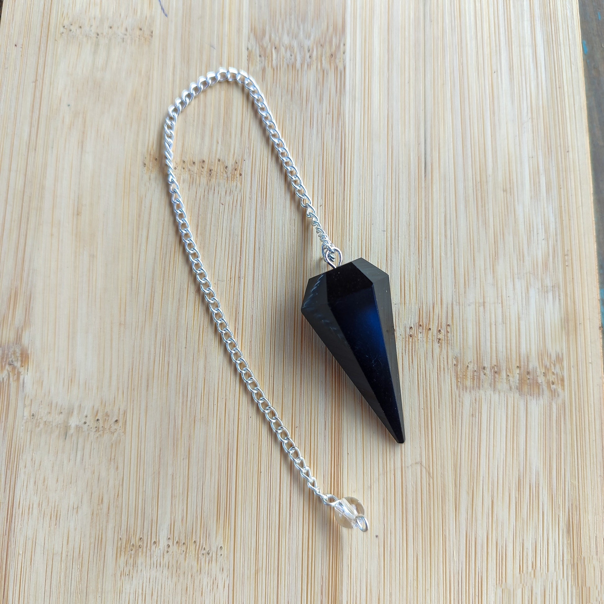 Vista completa de péndulo esotérico de obsidiana negra y cadena estirada para terapias energéticas.
