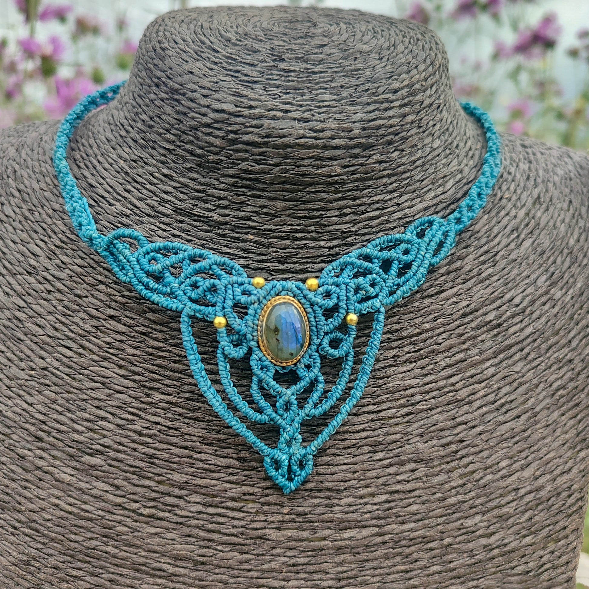 Primer plano de una gema labradorita con reflejos místicos engarzada a mano en joyería de macramé.