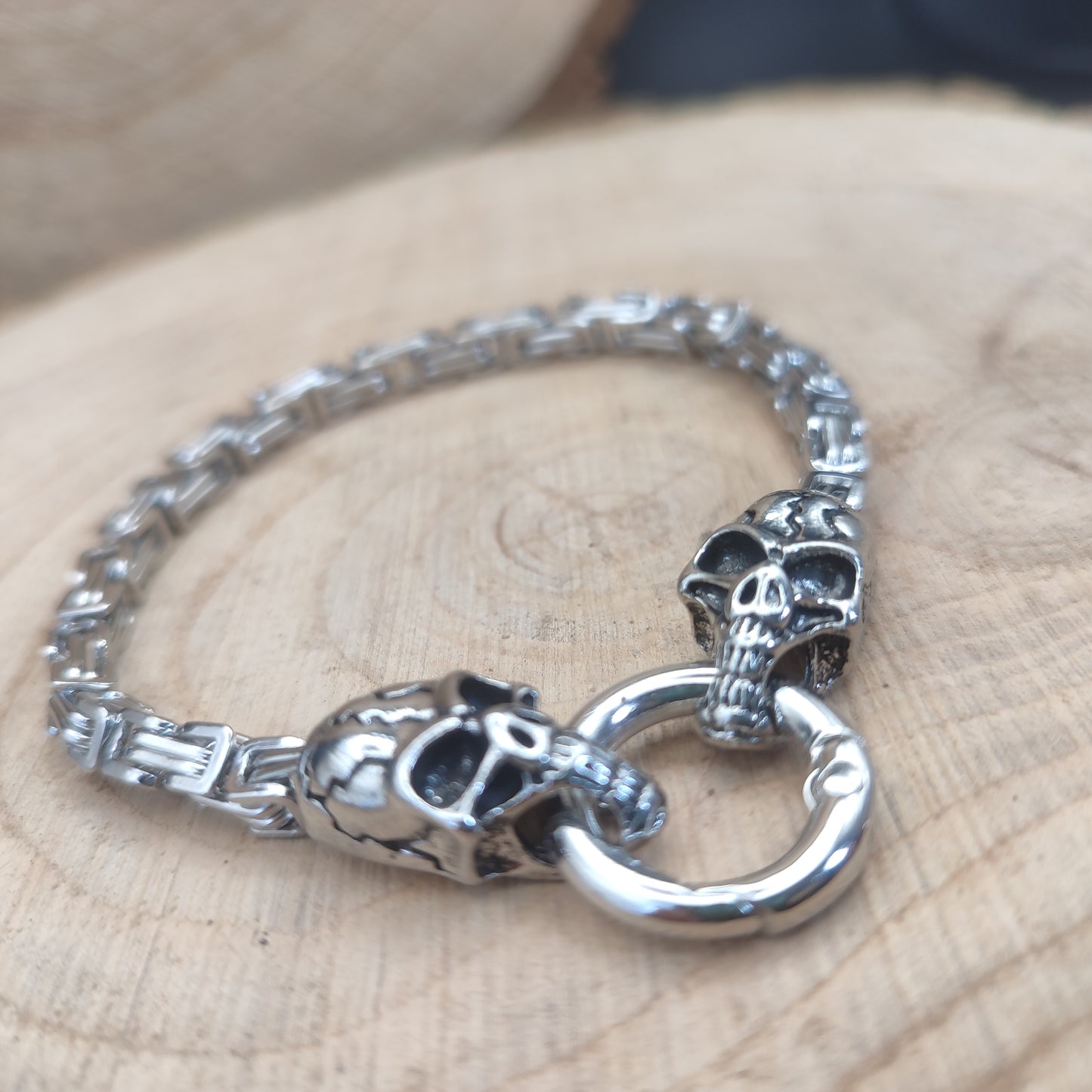 Pulsera de calaveras con cadena de acero y cierre circular sobre madera