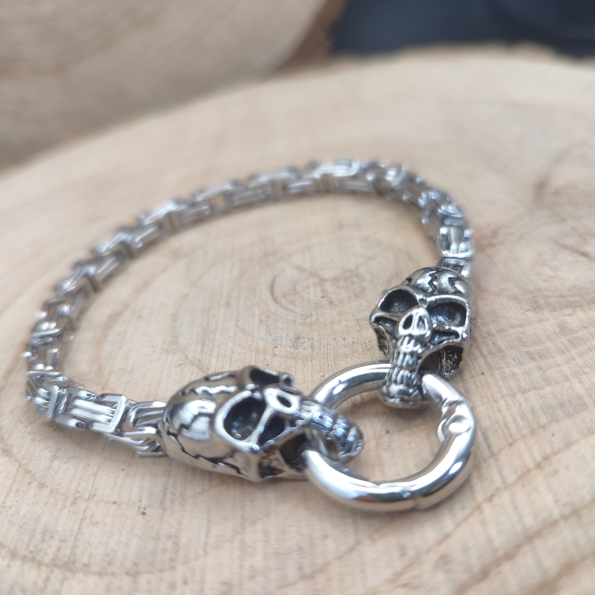 Pulsera de calaveras con cadena de acero y cierre circular sobre madera