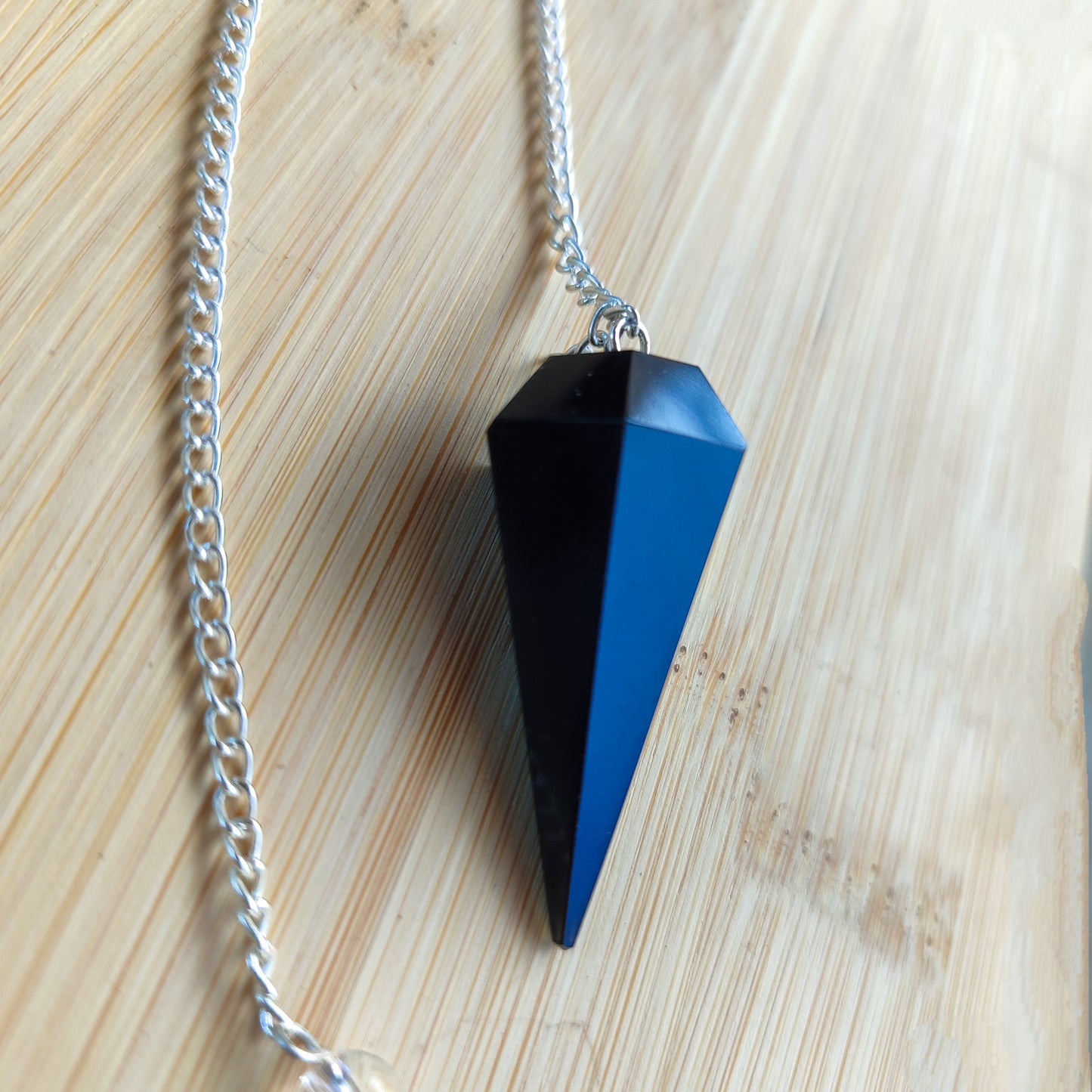 Péndulo de radiestesia de obsidiana negra colgado de su cadena mostrando su equilibrio perfecto.